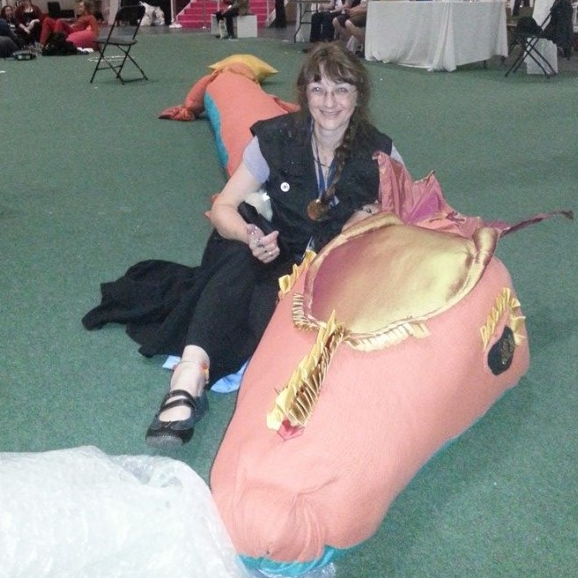 A photo of Serena Culfeather sitting astride a 12-foot long pink fabric dragon laid out on the floor.